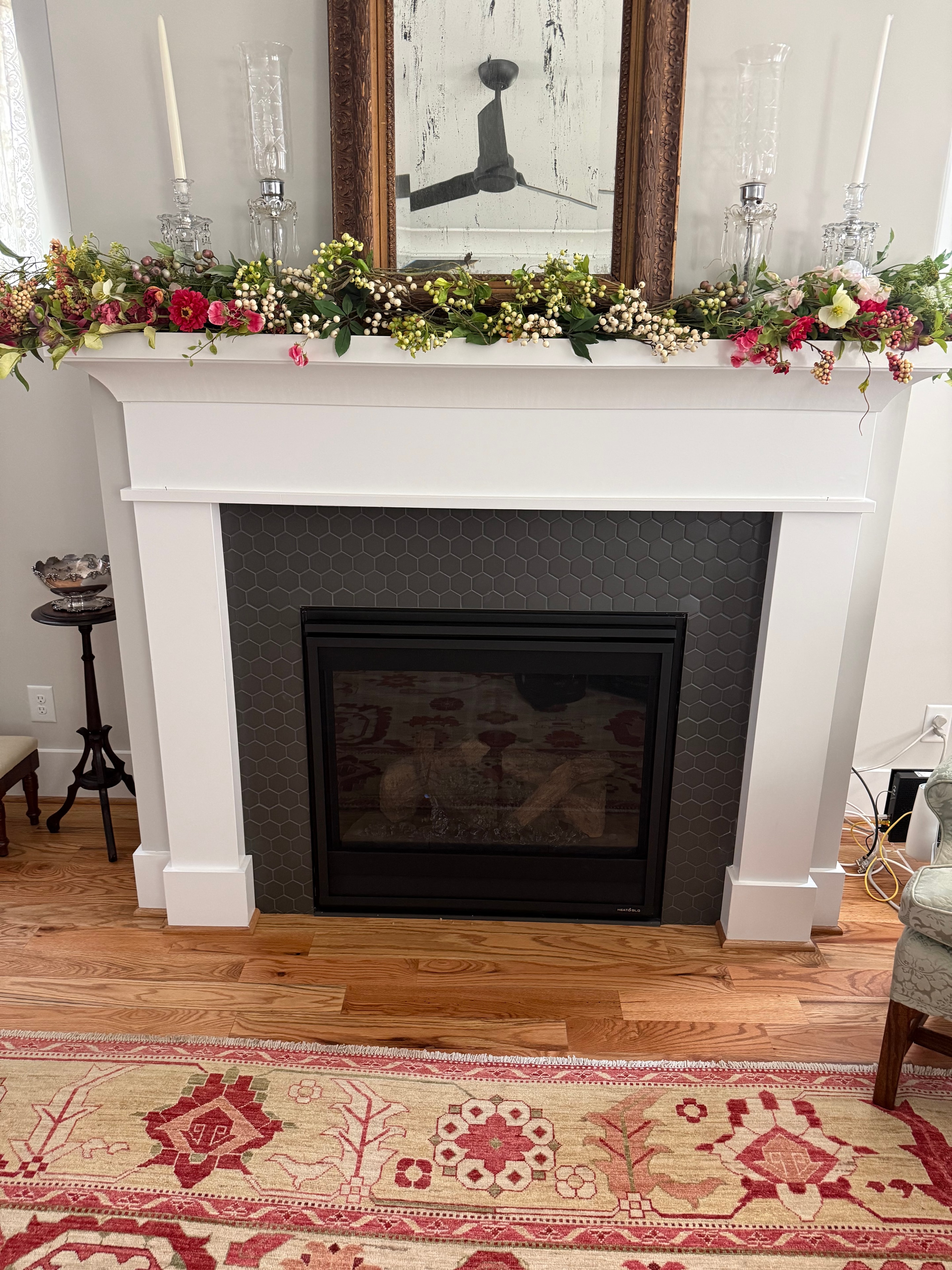 Gas fireplace with black hexagonal tile surround and white mantel decorated with floral garland