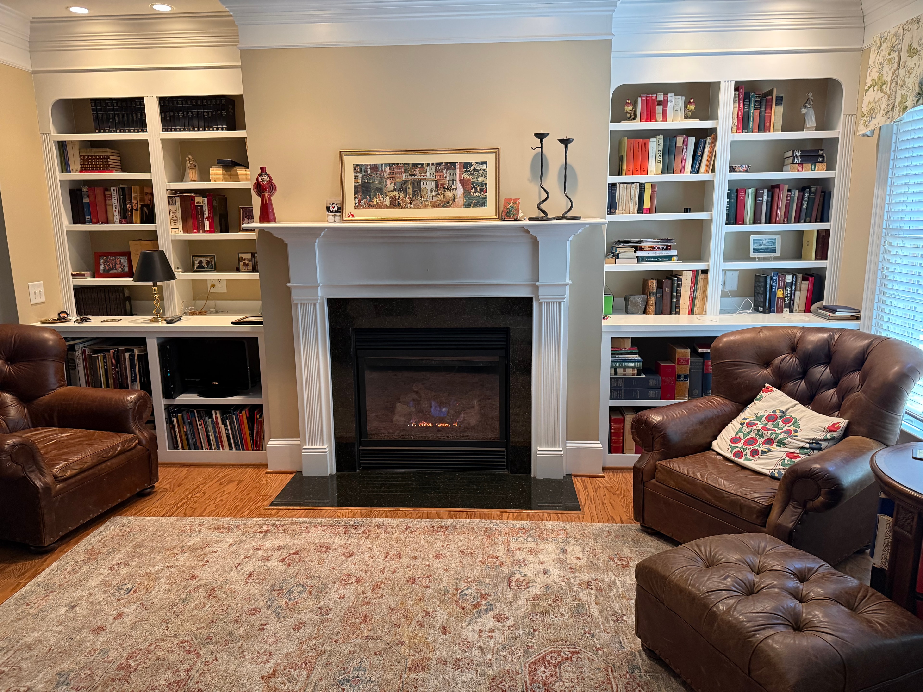 Gas fireplace with dark granite surround flanked by white built-in bookshelves and leather chairs